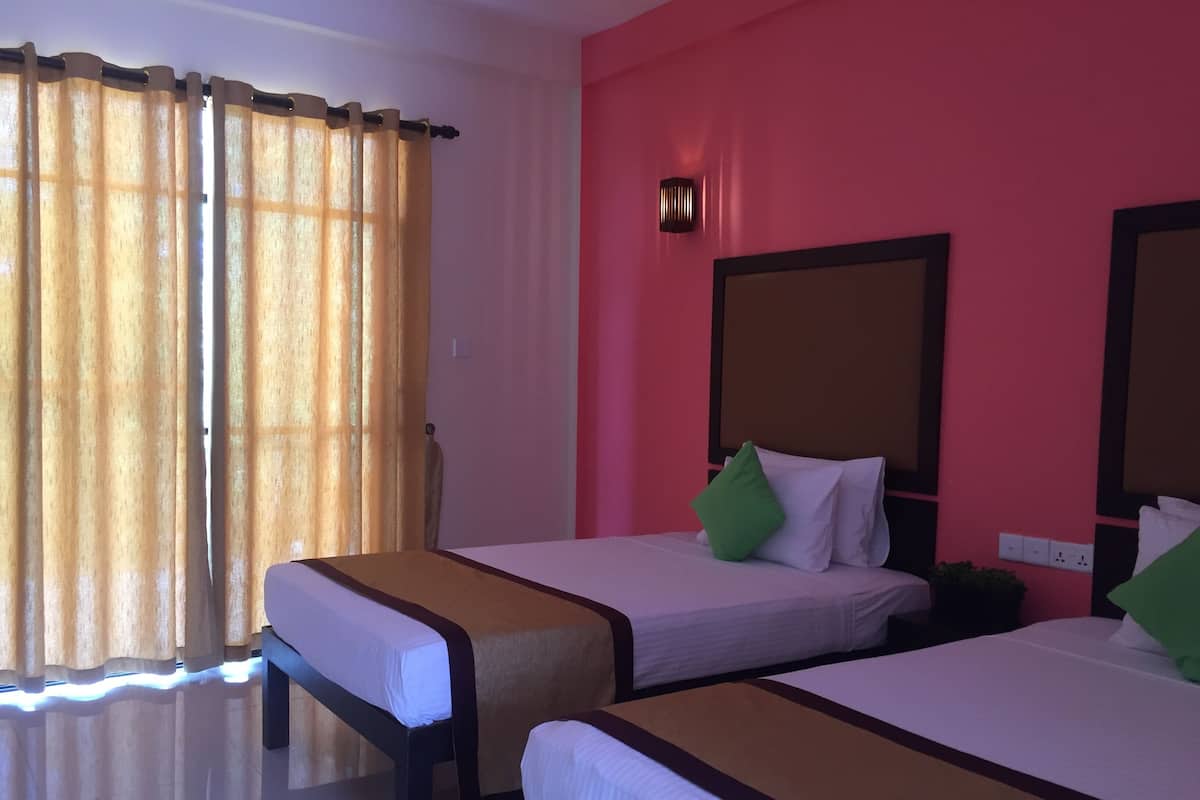 Une chambre d’hôtel avec deux lits, une grande fenêtre avec des rideaux, un luminaire fixé au mur et une prise de courant.