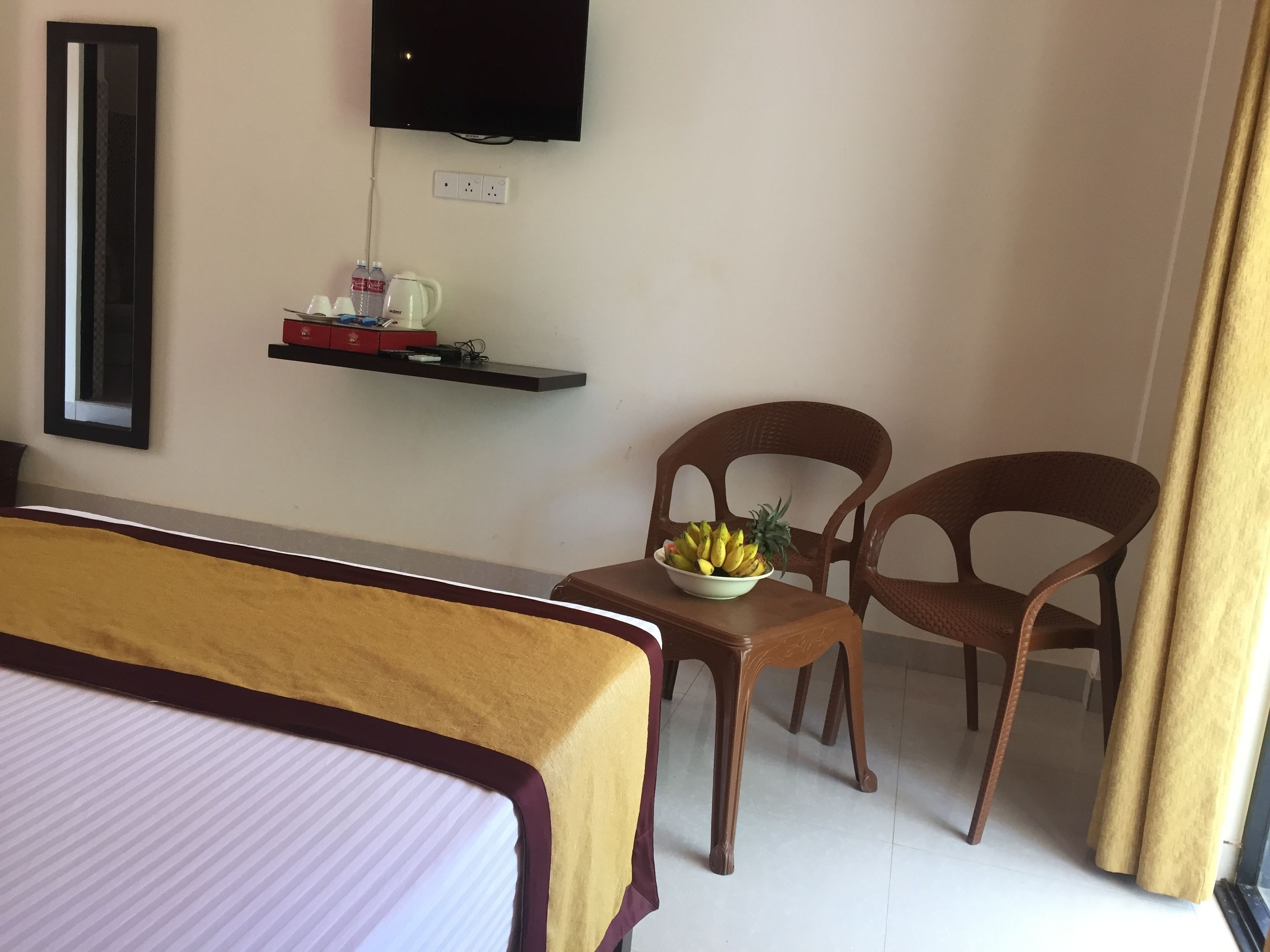 Een hotelkamer met een bed, een aan de muur bevestigde televisie, een tafeltje met een schaal fruit en twee stoelen.