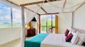A bedroom with a bed, a nightstand, a chair, a table, and a view of the outdoors. - Organic Garden Sigiriya (Avudangawa)