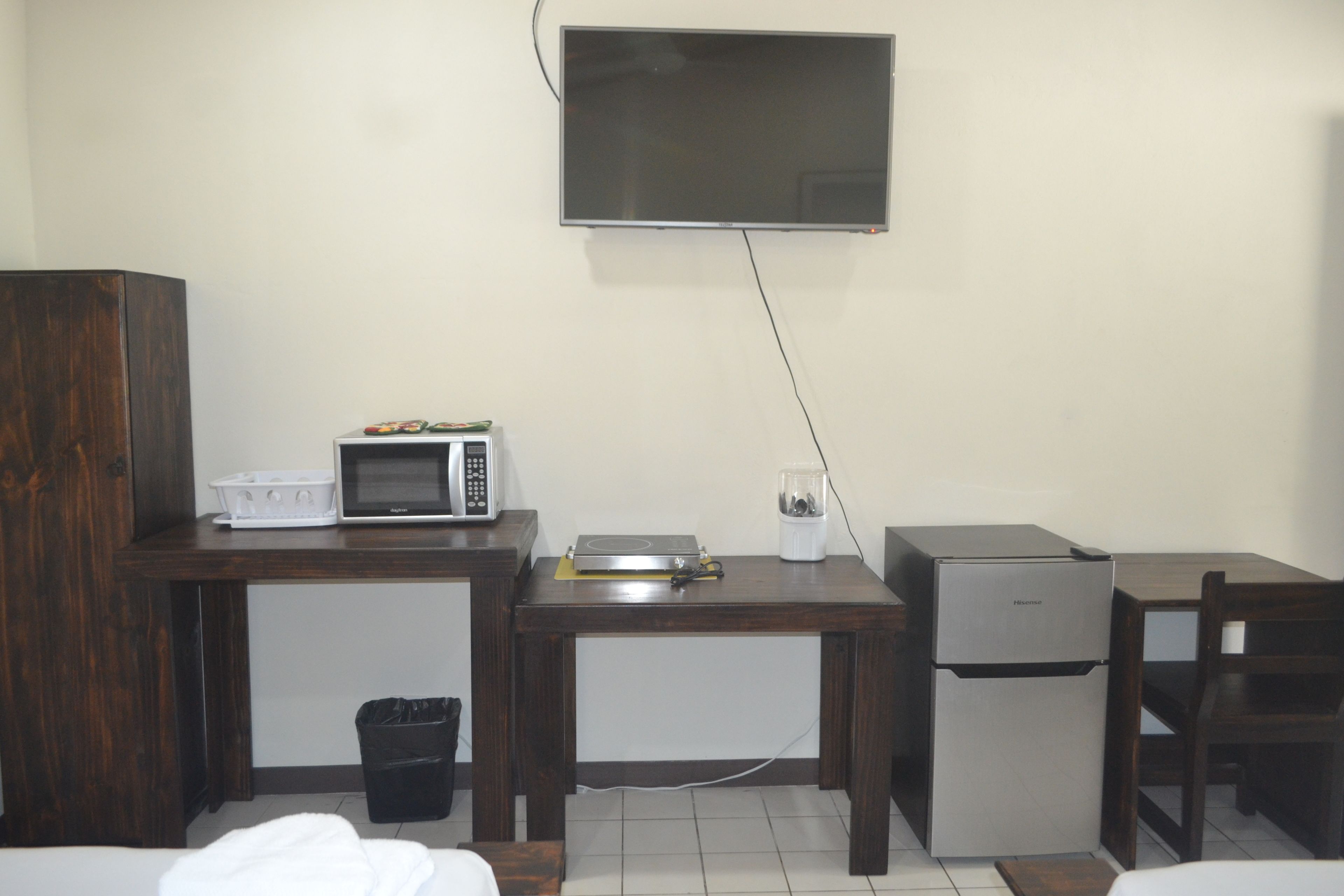A compact room with a wooden desk, a microwave, a small refrigerator, and a TV mounted on the wall.