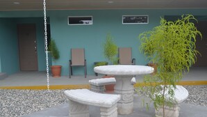 Un'area patio con un tavolo in pietra e panche, circondata da piante in vaso e un'altalena in rete metallica.