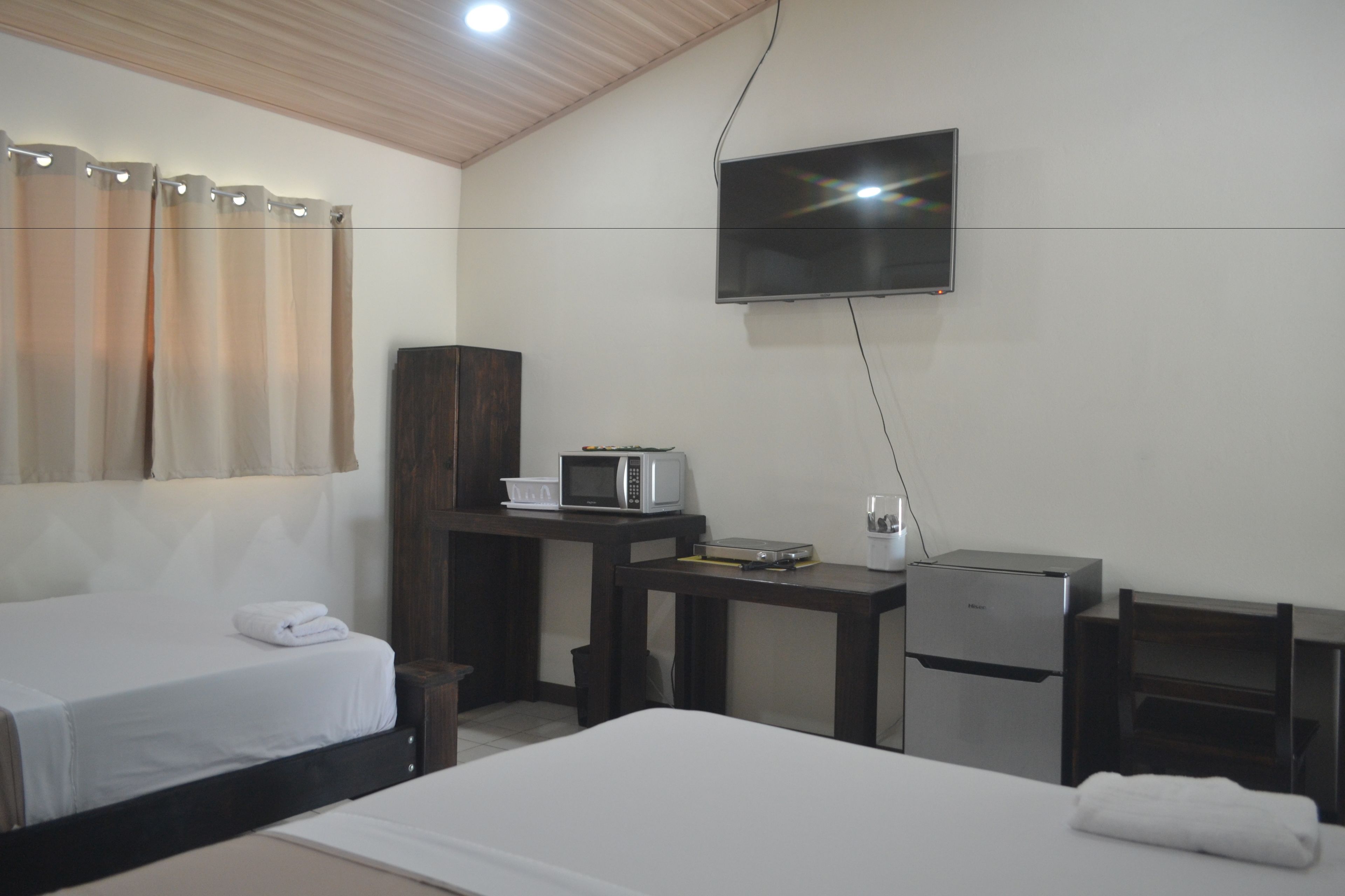 Une chambre d’hôtel avec deux lits, un téléviseur fixé au mur, un four à micro-ondes, un petit réfrigérateur et un bureau en bois.