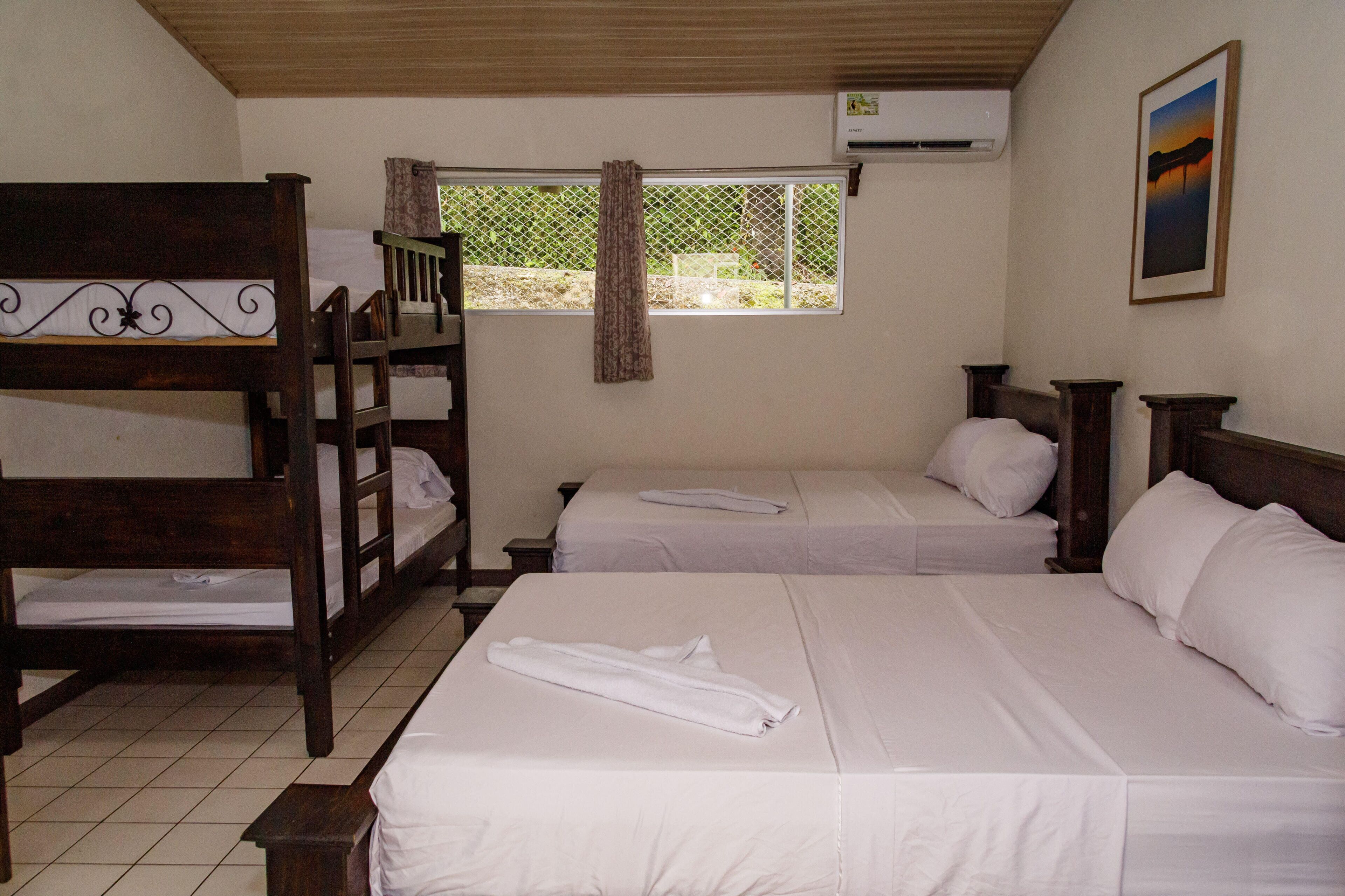 A room with two single beds, a bunk bed, and a window with curtains.