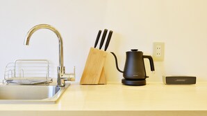 A kitchen with a stainless steel sink, a wooden knife block, a black electric kettle, and a small speaker on the countertop. - HOSTEL nid OSAKA (Osaka)