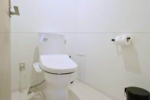 Eine weiße Toilette mit Bedienfeld, Toilettenpapierhalter an der Wand und einem schwarzen Mülleimer.