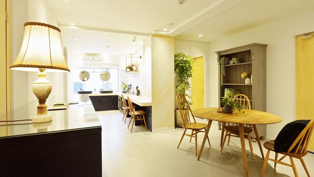 A modern kitchen with a dining area, featuring a round wooden table, chairs, and a lamp. - HOSTEL nid OSAKA (Osaka)