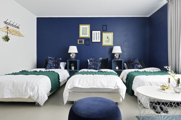 Ein modernes Schlafzimmer mit drei Betten, einem runden Tisch und einer blauen Akzentwand.