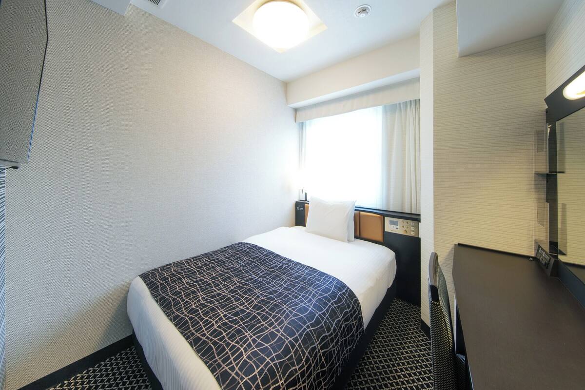 Una habitación de hotel con cama, mesita de noche, espejo y ventana con cortinas.