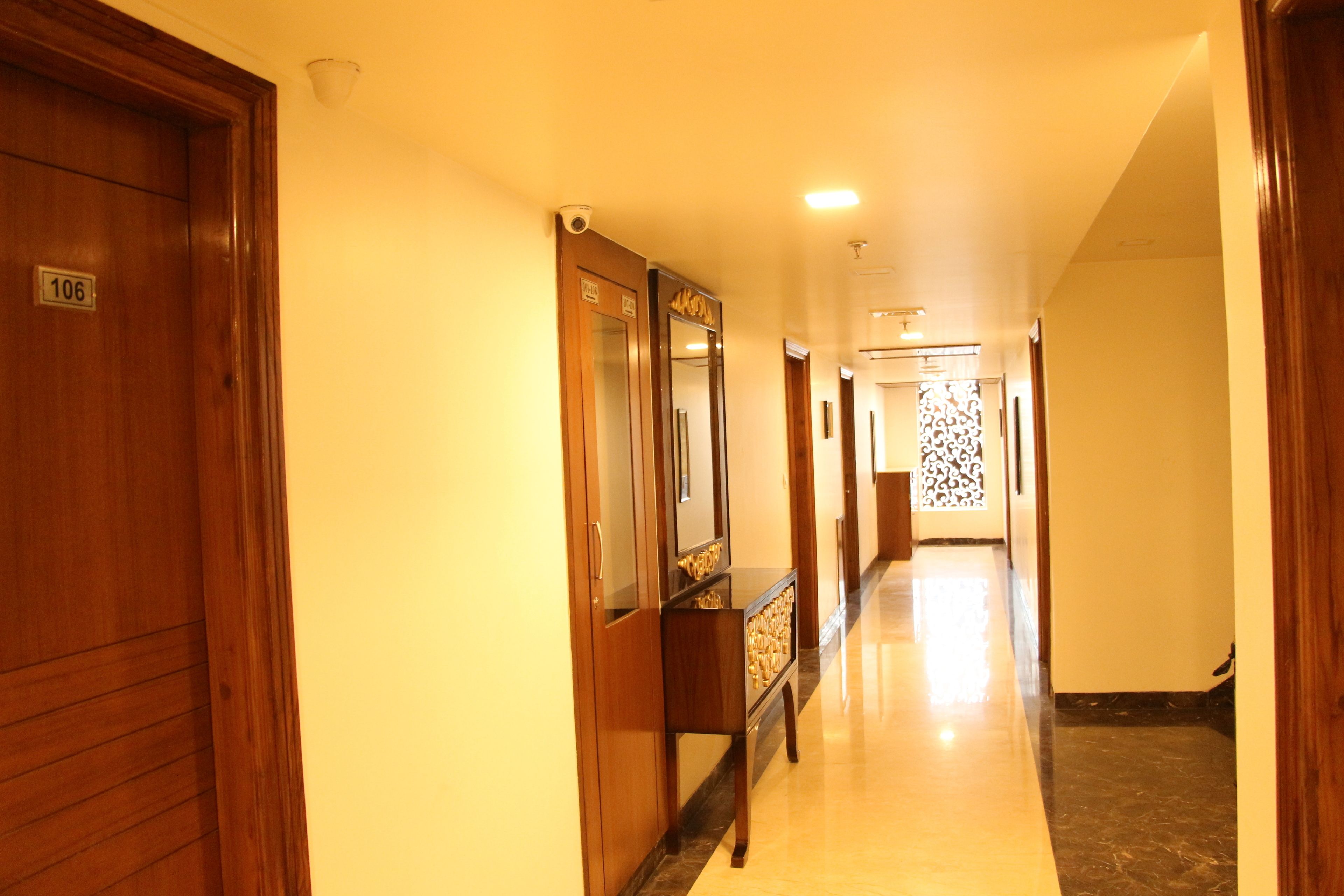 A hotel hallway with wooden doors, a marble floor, and a security camera.
