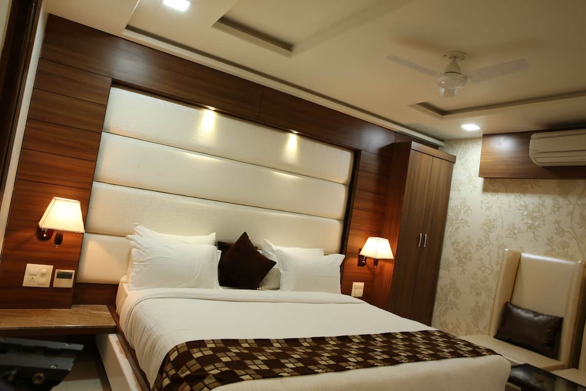 A hotel room with a large bed, wooden headboard, two bedside lamps, a ceiling fan, and an air conditioning unit.
