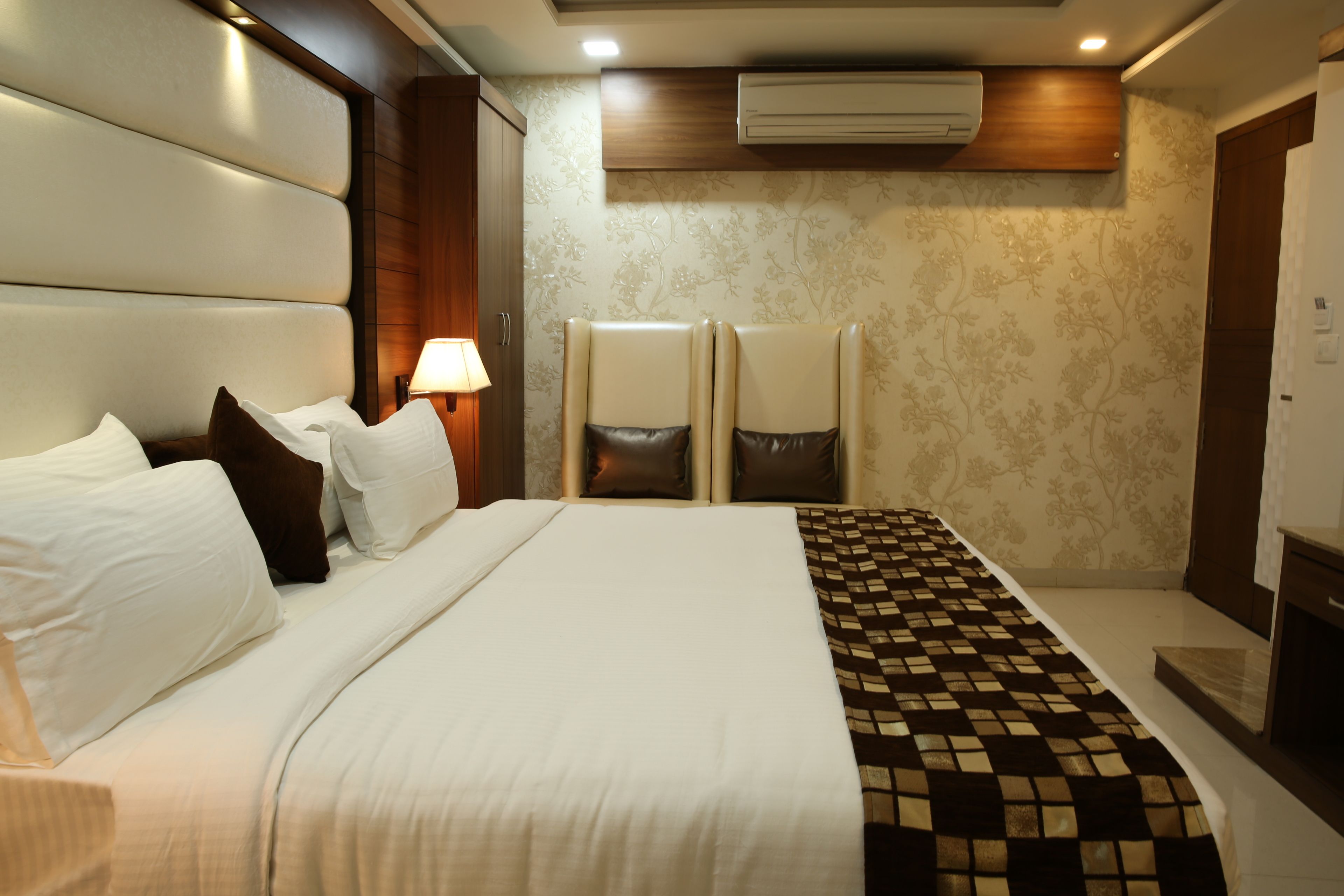 Een hotelkamer met een groot bed, twee fauteuils, een nachtkastje en een airconditioning.