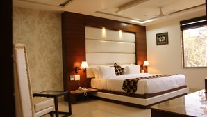 A modern hotel room with a large bed, bedside lamps, a nightstand, a chair, and a view of the outdoors. - Kc Inn (Ajmer)
