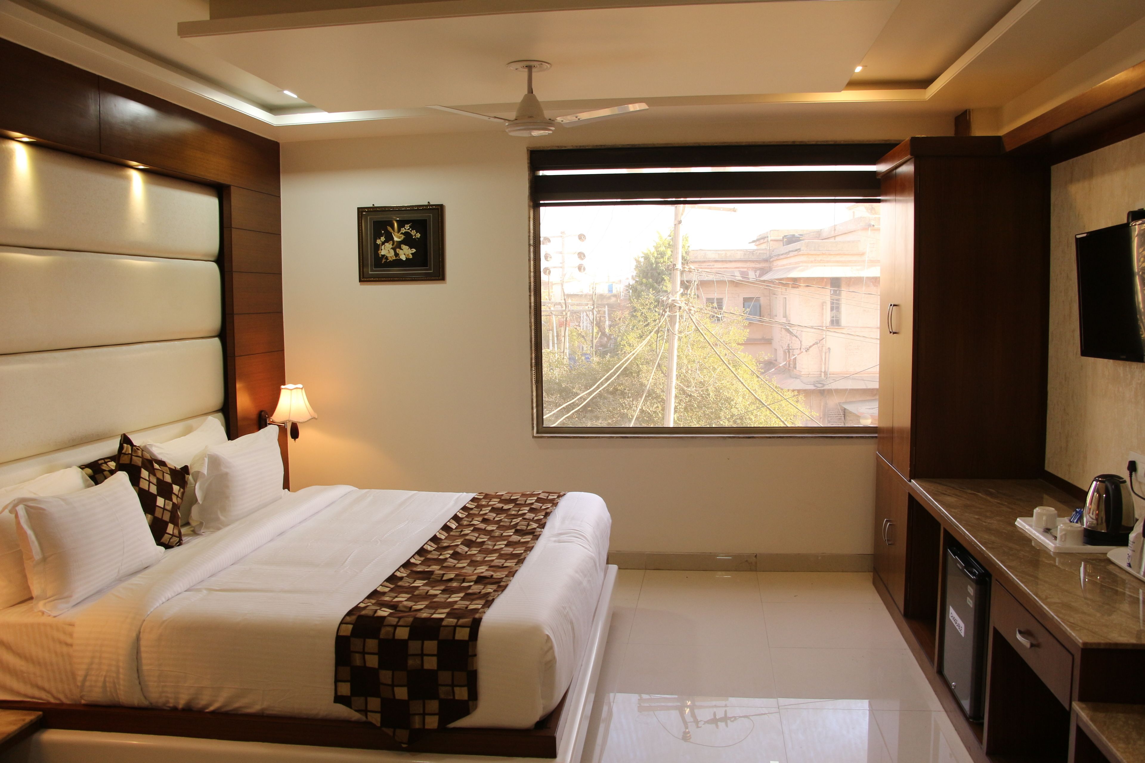 Quarto de hotel com cama, luminária de cabeceira, janela com vista e uma pequena área de cozinha.