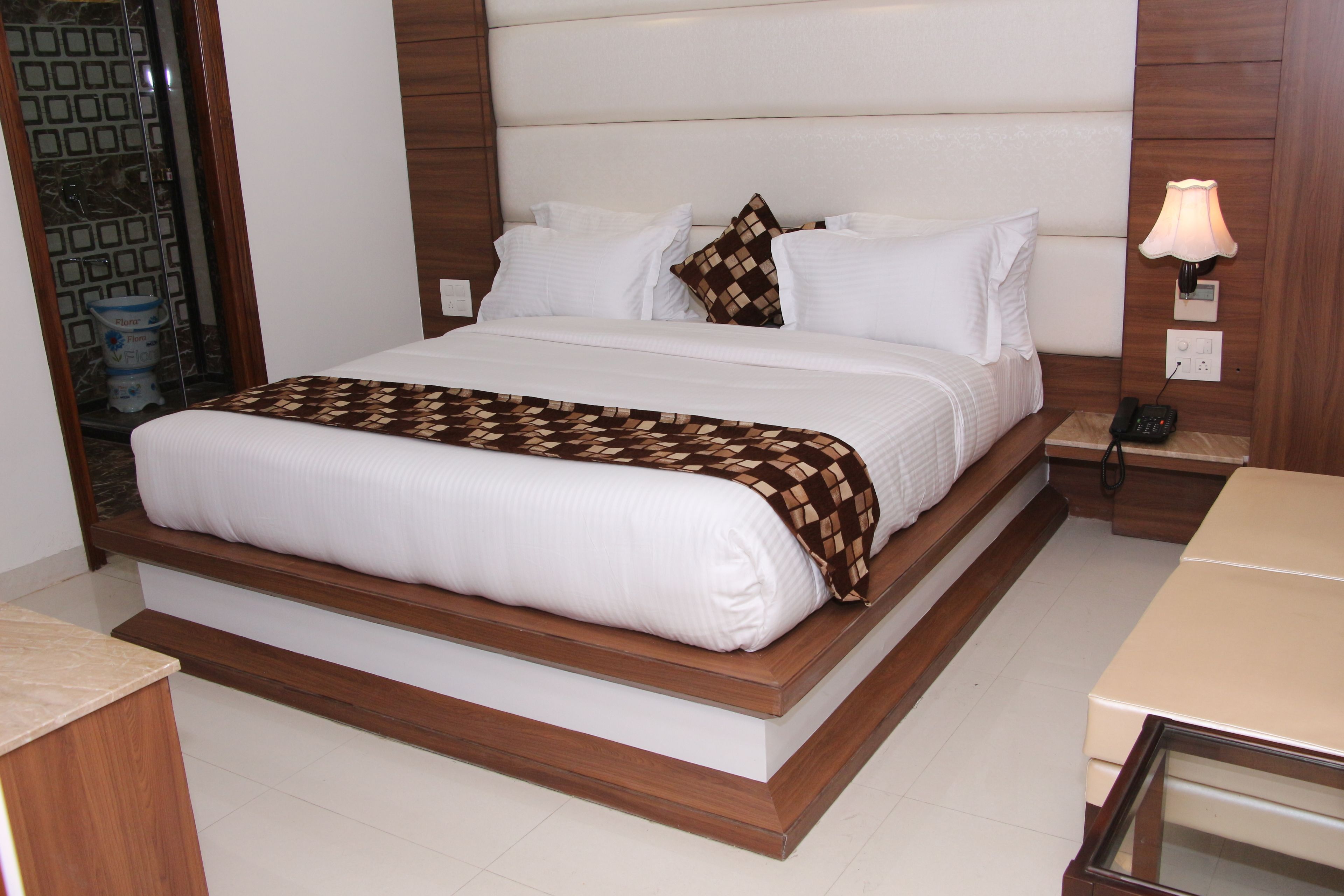 A neatly made bed with a patterned throw, a bedside table with a lamp, and a wall-mounted phone.