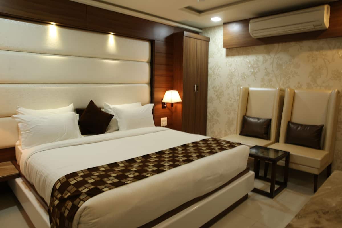 A hotel room with a large bed, a nightstand, a lamp, a wardrobe, and two armchairs.