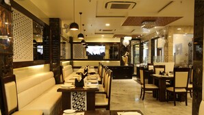 A restaurant with a long counter, cushioned seating, and a television screen. - Kc Inn (Ajmer)