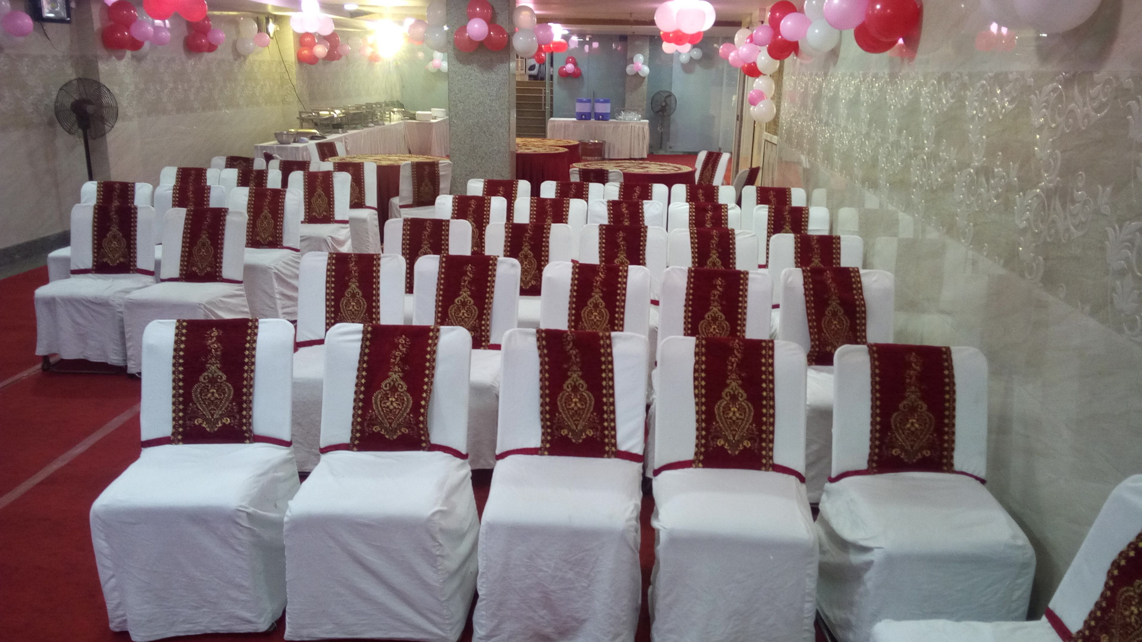 Rows of white chairs with red and gold sashes, arranged in a hall with a red carpet.