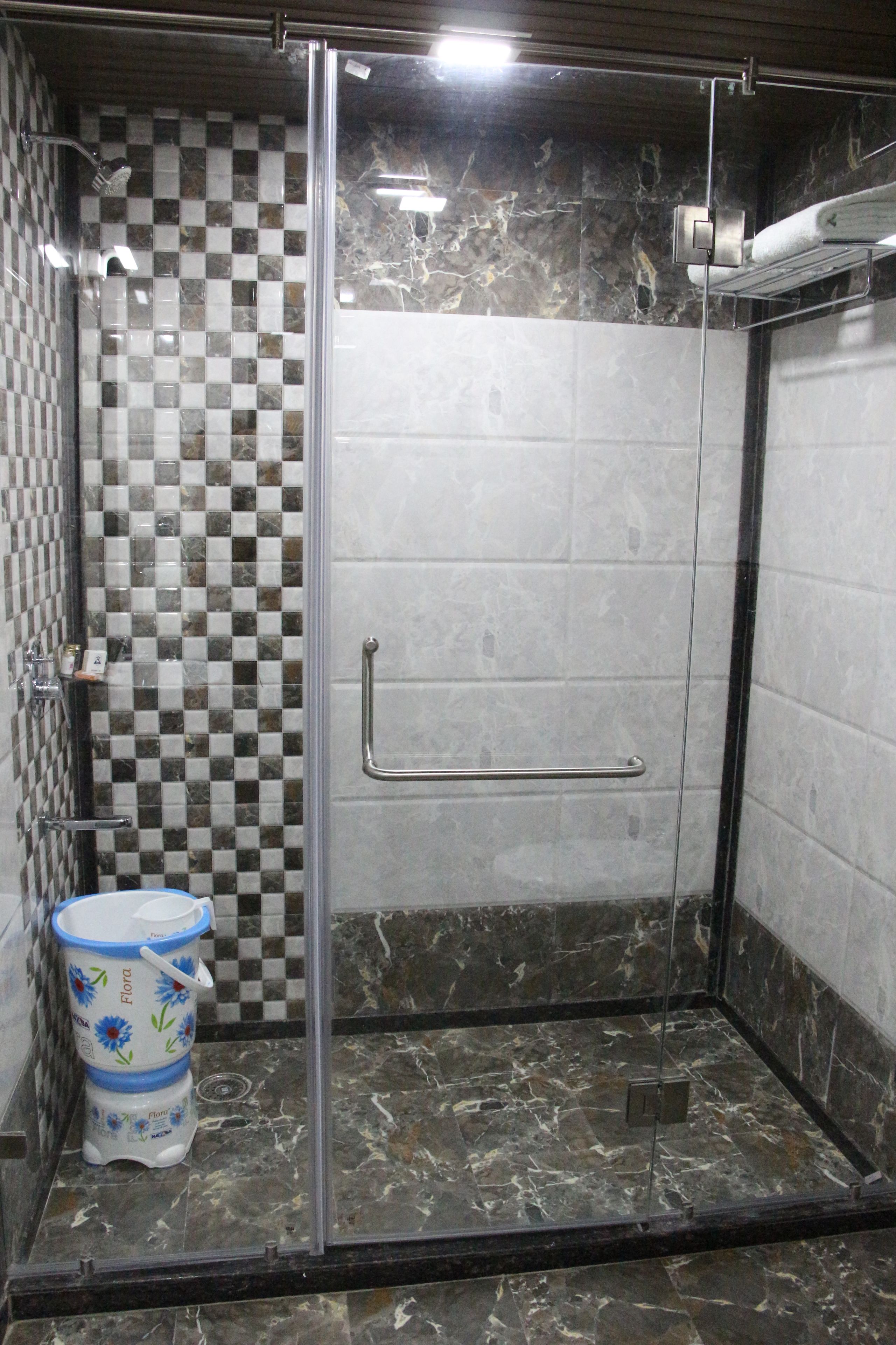 A glass-enclosed shower with a checkered tile wall, a handrail, and a marble floor.