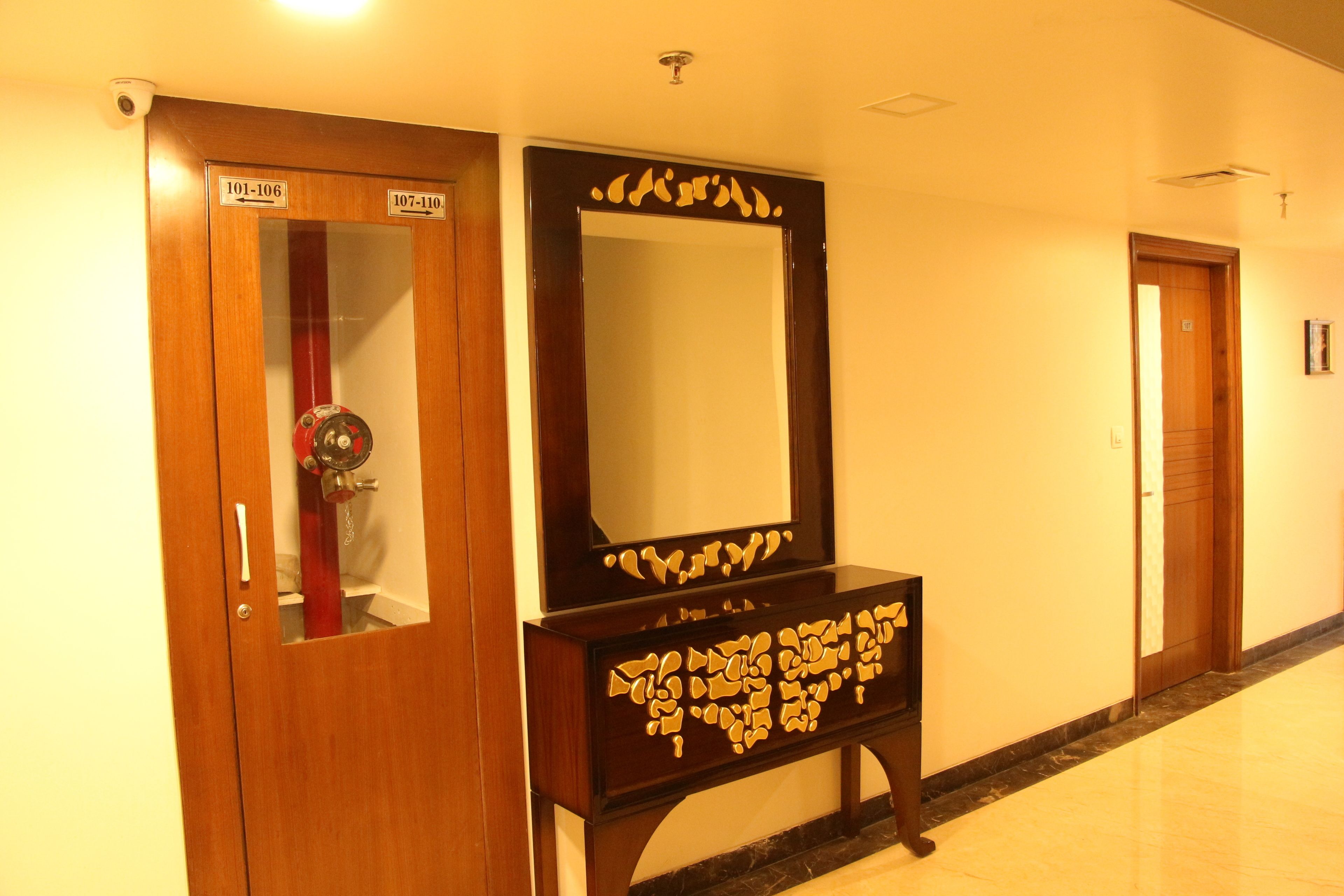 A hallway with wooden doors labeled 101-106 and 107-110, a large mirror with a decorative frame, and a marble floor.