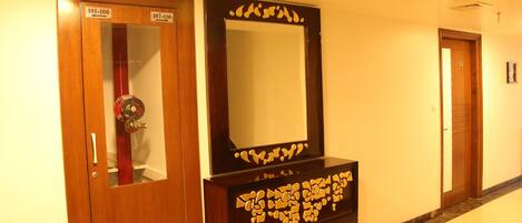 A hallway with wooden doors labeled 101-106 and 107-110, a large mirror with a decorative frame, and a marble floor.