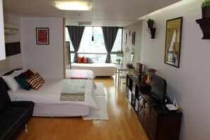 Quarto de hotel moderno com uma cama grande, uma escrivaninha, uma televisão e vista para a cidade pela janela.