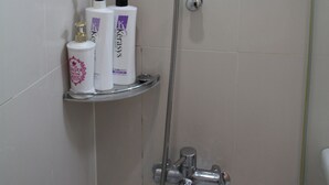 Une douche équipée d’un pommeau de douche à main et d’un robinet mural. Deux bouteilles sont posées sur une étagère située sous la douche.