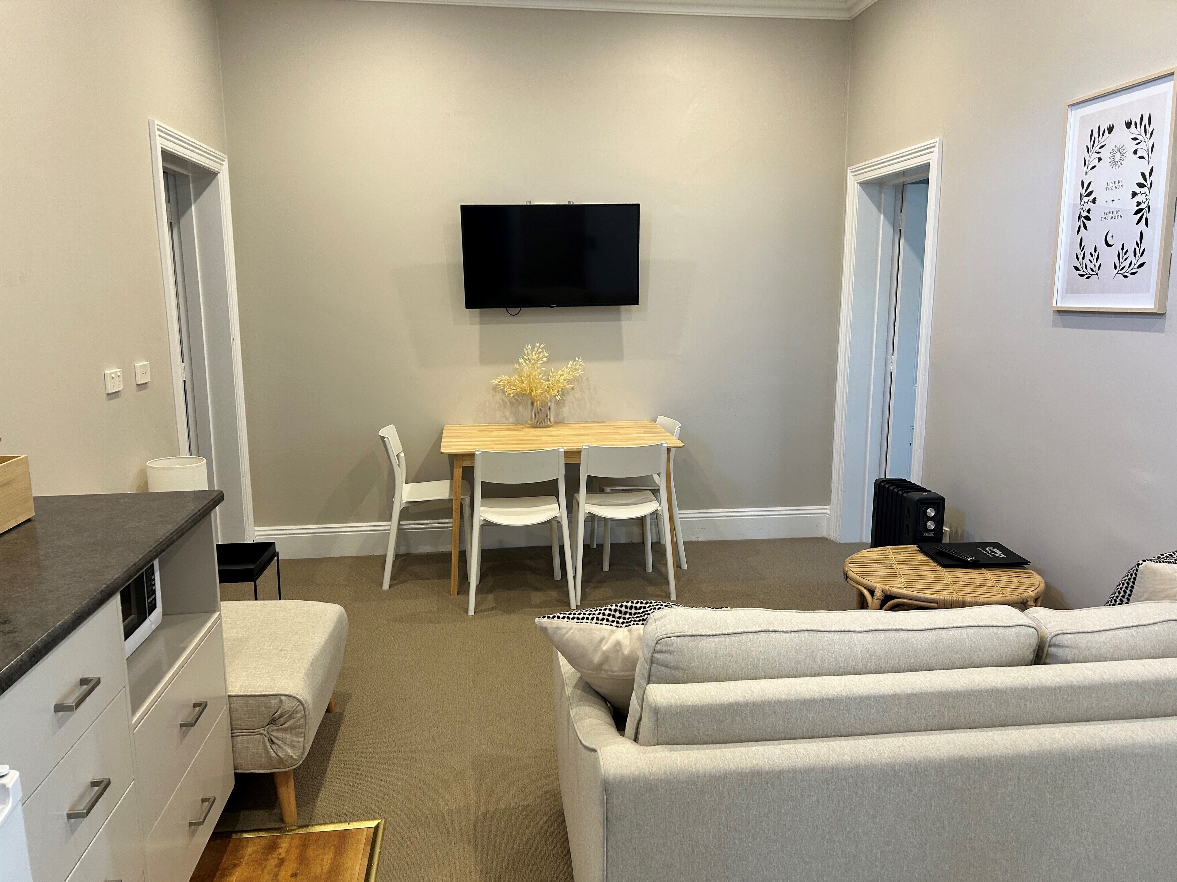 A compact living space with a kitchenette, a dining area, a sofa, and a flat-screen TV mounted on the wall.