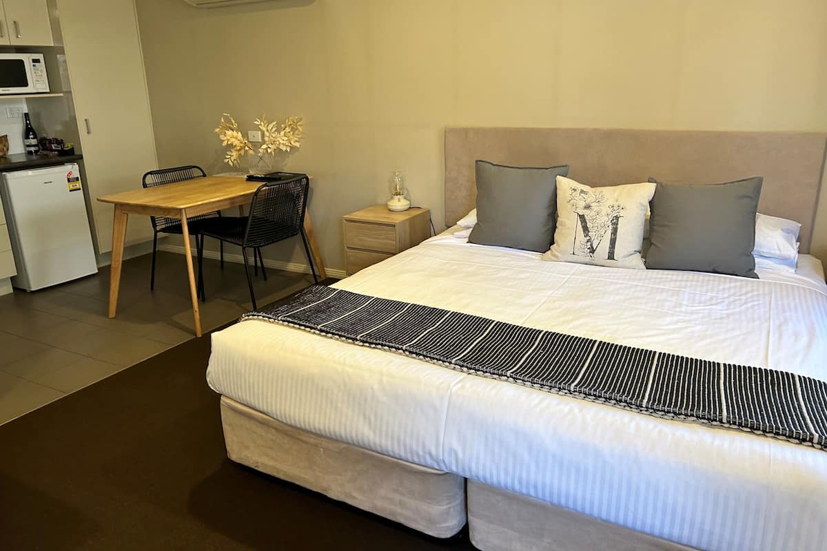 A hotel room with a large bed, a wooden desk, a chair, a small table, and a microwave.