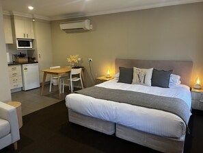 A bedroom with a large bed, bedside tables with lamps, a desk with a chair, and a kitchenette with a microwave and refrigerator. - Millthorpe Boutique Motel (Millthorpe)