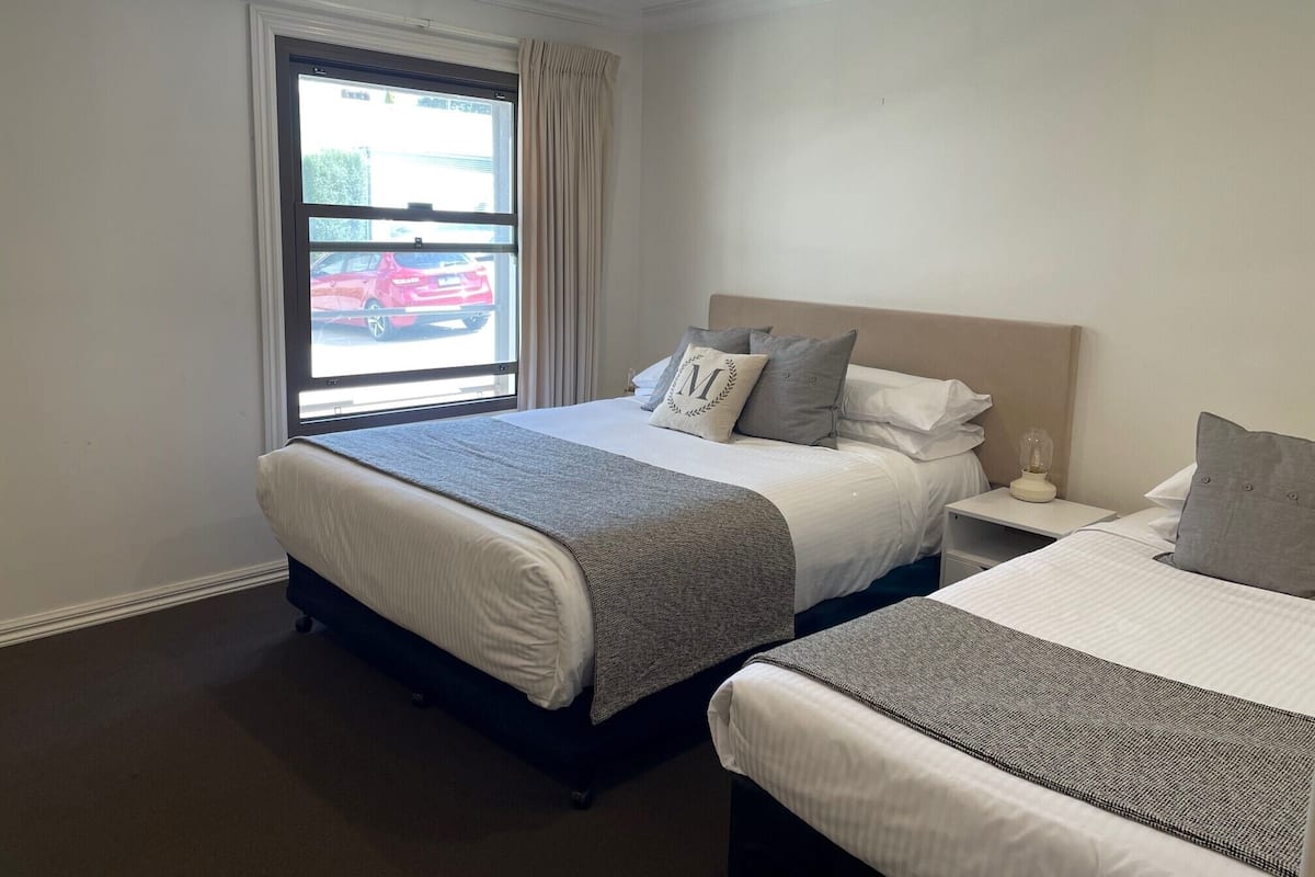 A hotel room with a large bed, a smaller bed, a nightstand with a lamp, and a window with curtains.