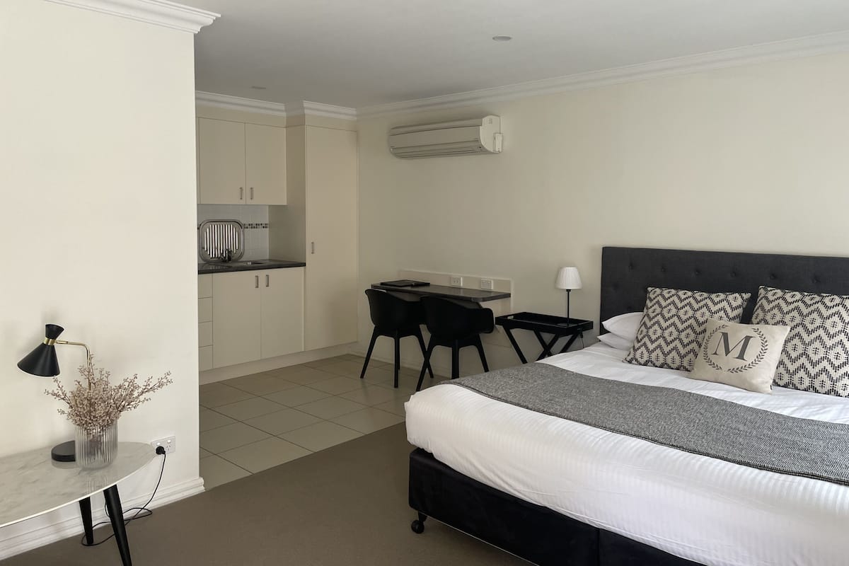 A bedroom with a bed, bedside table, lamp, and a small desk with a chair.