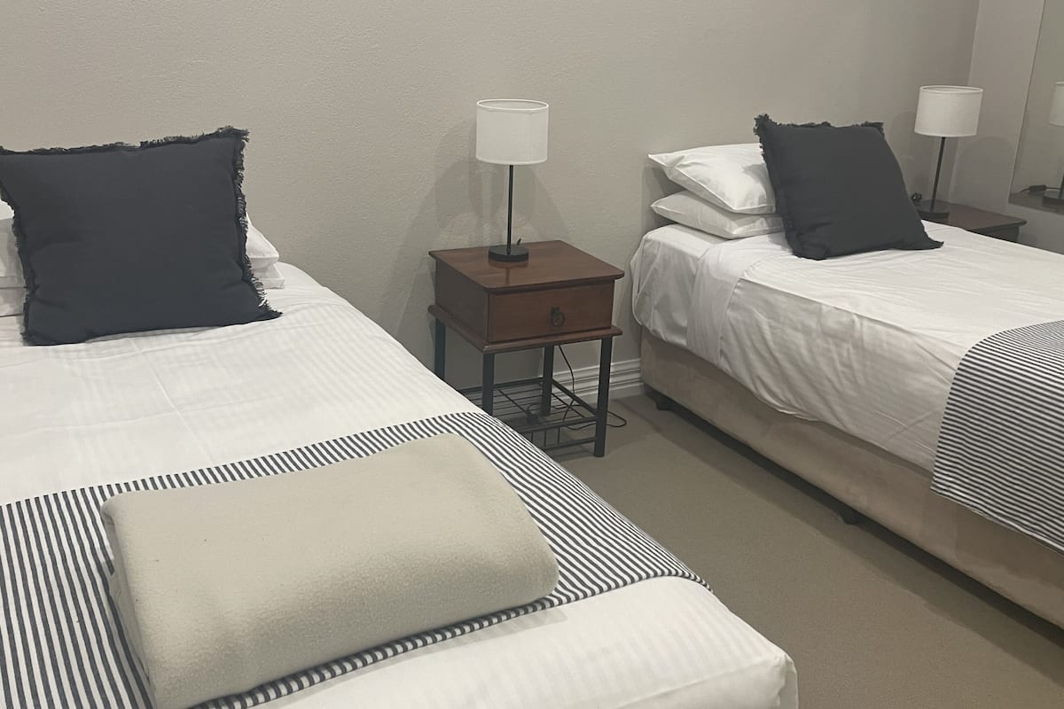 A hotel room with two beds, each with a pillow and a lamp on a side table.