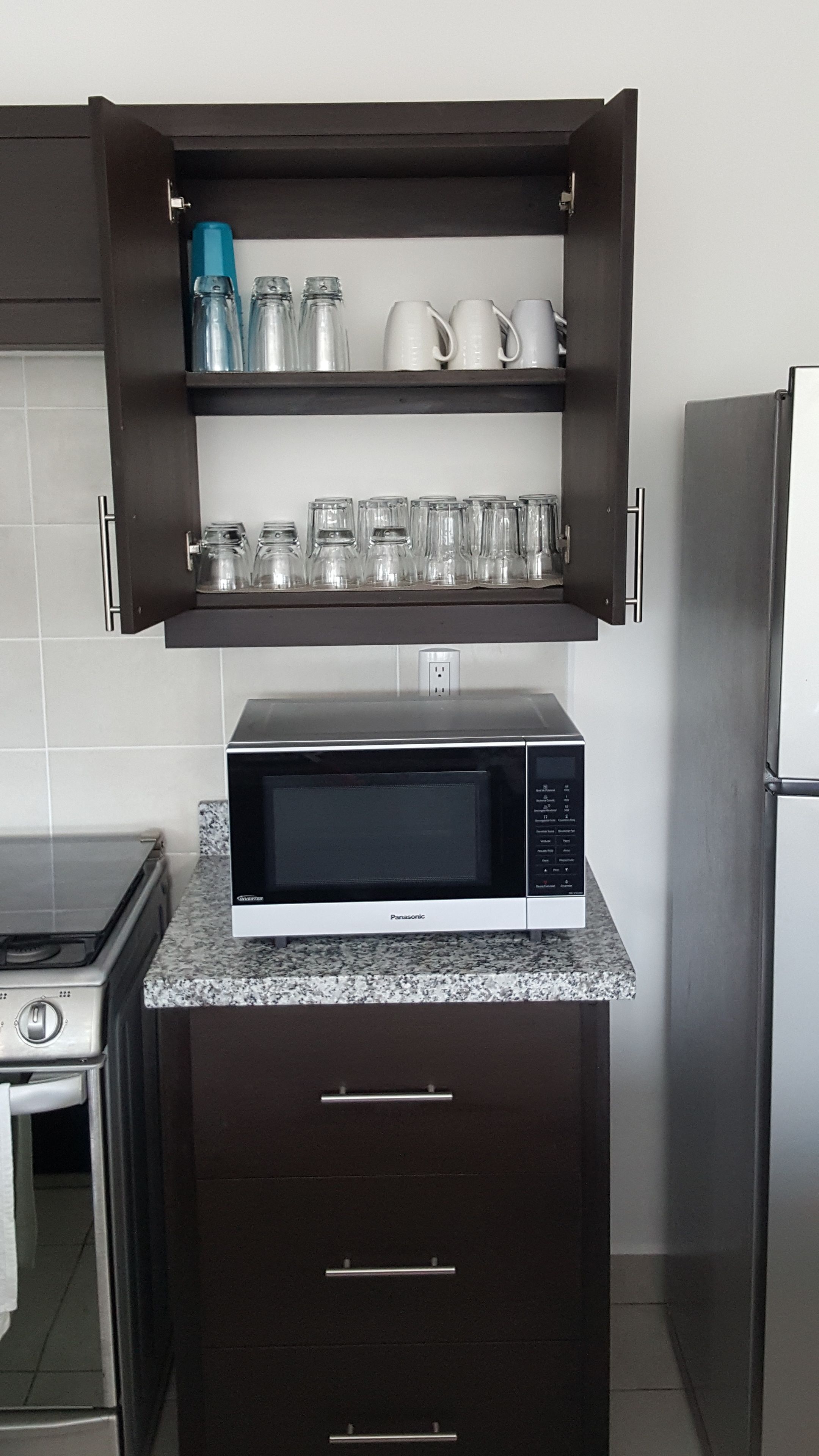 A kitchen with a microwave on a granite countertop, a stove, and a refrigerator.