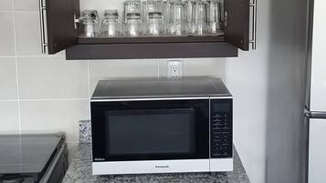 A kitchen with a microwave on a granite countertop, a stove, and a refrigerator.