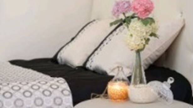 A bed with a white and black patterned bedspread, two pillows, a vase with flowers, and a small candle on a bedside table. - Gangnam Rodem (Seoul)