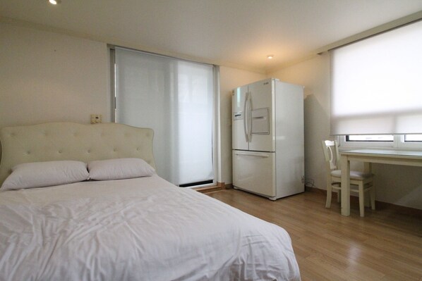 A bedroom with a bed, a refrigerator, a desk, and a chair.