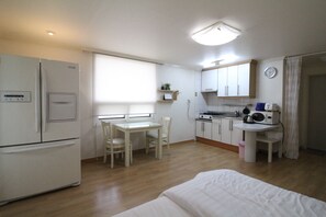 Eine kleine Küche mit Kühlschrank, Herd, Mikrowelle und Spüle. Ein Esstisch mit Stühlen und ein Fenster sorgen für natürliches Licht.