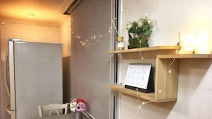 A dining area with a table set for two, a refrigerator, a shelf with a calendar, and decorative lights. - Gangnam Rodem (Seoul)