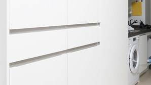 A modern kitchen with white cabinets, a washing machine, and a yellow shelf. - Ivory Central Gangnam (Seoul)