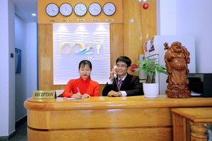 A reception desk at the COZY HOTEL with clocks displaying times in London, New York, Ha Noi, Moscow, and Paris.