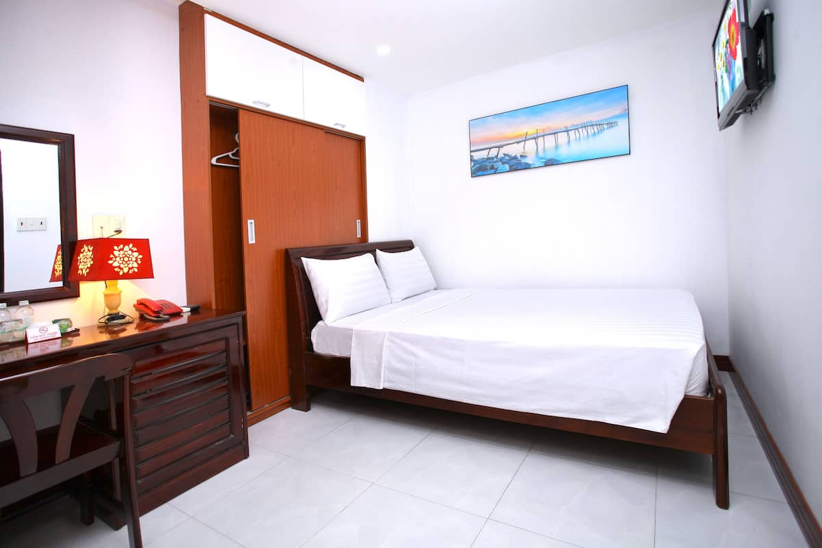 Quarto com cama, escrivaninha com luminária, telefone e guarda-roupa.