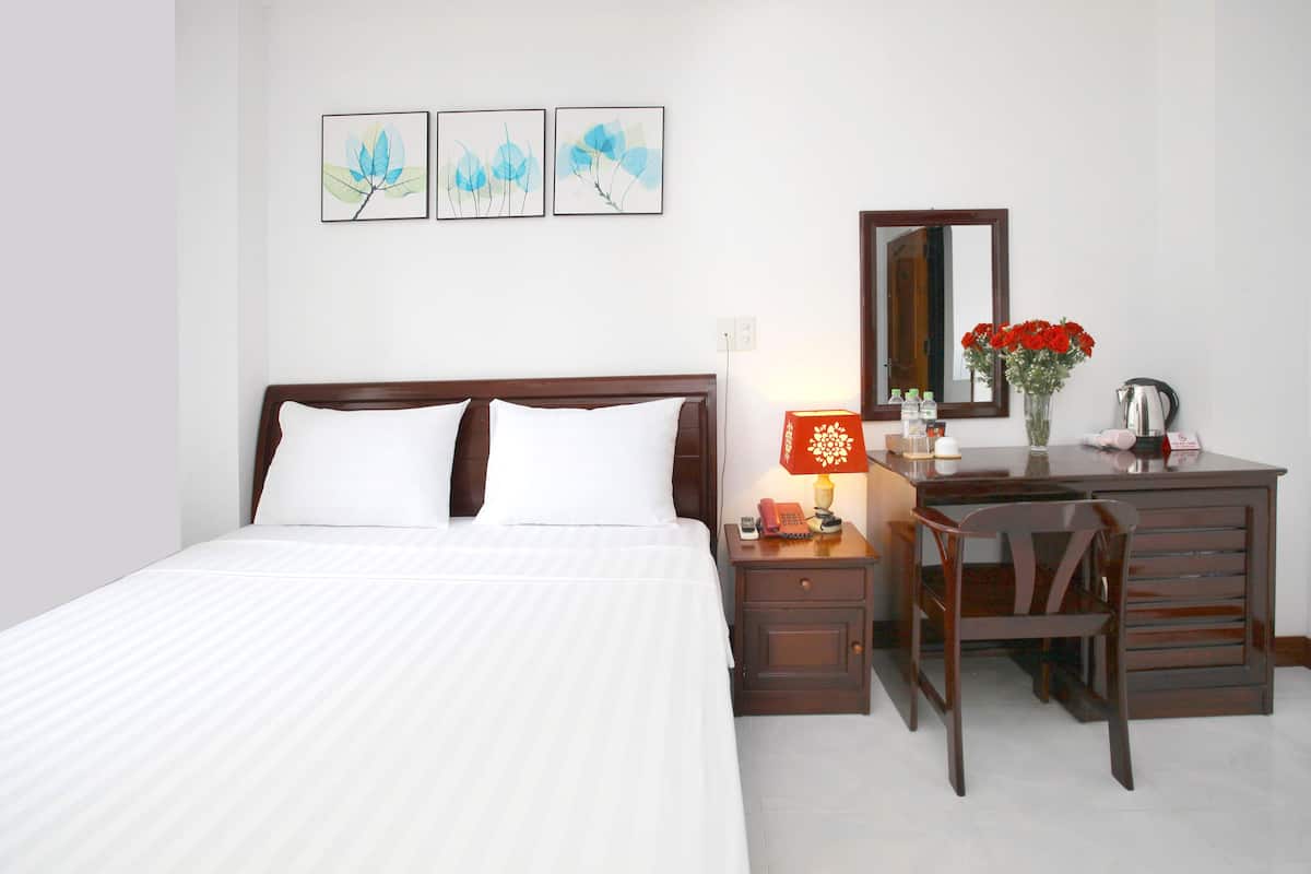 Quarto de hotel bem arrumado, com cama, mesa de cabeceira, escrivaninha, cadeira e espelho.