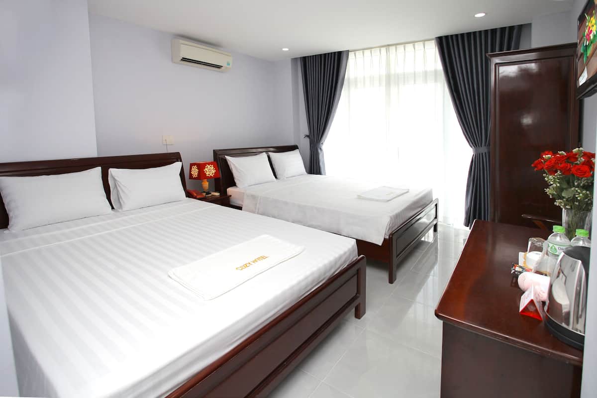 Quarto de hotel com duas camas, uma escrivaninha com artigos de higiene pessoal e uma janela grande com cortinas.