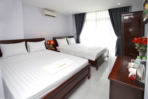 A hotel room with two beds, a desk with toiletries, and a large window with curtains.