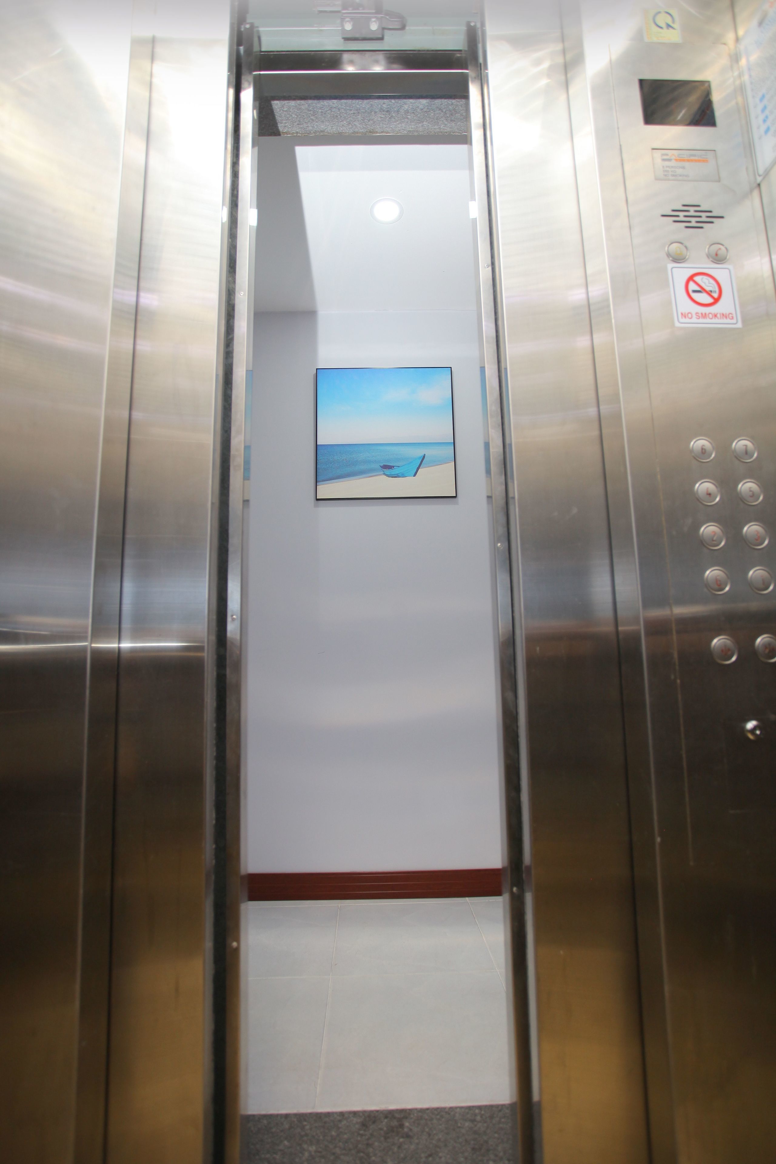 An elevator interior with a stainless steel finish, a no-smoking sign, and a small picture of a beach scene on the wall.