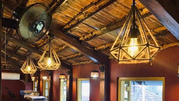A cozy restaurant with wooden tables and benches, exposed wooden beams, and hanging light fixtures. - Marquito's Guest House (Panaji)