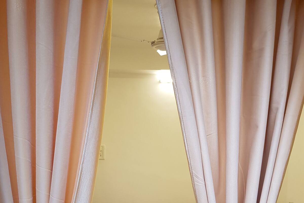 Un dormitorio con una cama, una toalla enrollada y cortinas.