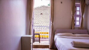 A bedroom with a bed, a small bedside table, a chair, and a view of a tiled balcony. - Marquito's Guest House (Panaji)
