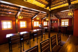 A restaurant with wooden tables and benches, a thatched roof, and hanging light fixtures.