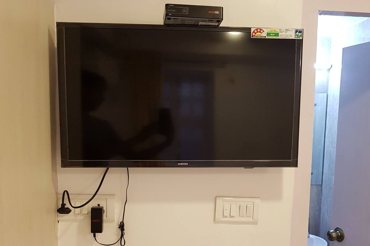 Televisor de pantalla plana montado en la pared, con un enchufe y un interruptor de luz debajo.